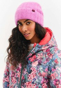 Kvetovaná prešívaná bunda s tmavomodrým základom, ružovými a fialovými kvetmi; jednofarebná ružová pletená čiapka s textúrovaným vzorom a hnedou nášivkou.