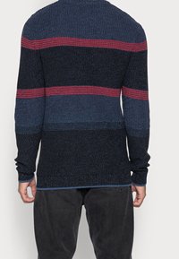 Maglione lavorato a maglia con maniche lunghe, caratterizzato da un design a righe nei colori blu navy, blu e rosso. Tessuto testurizzato con colletto rotondo e polsini a coste.
