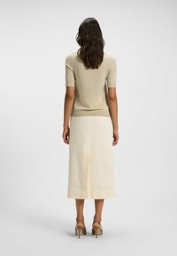 Ljust beige kortärmad topp med mjuk textur, ihopparad med en krämfärgad knälång kjol med en slits bak. Bruna sandaler med öppen tå syns.