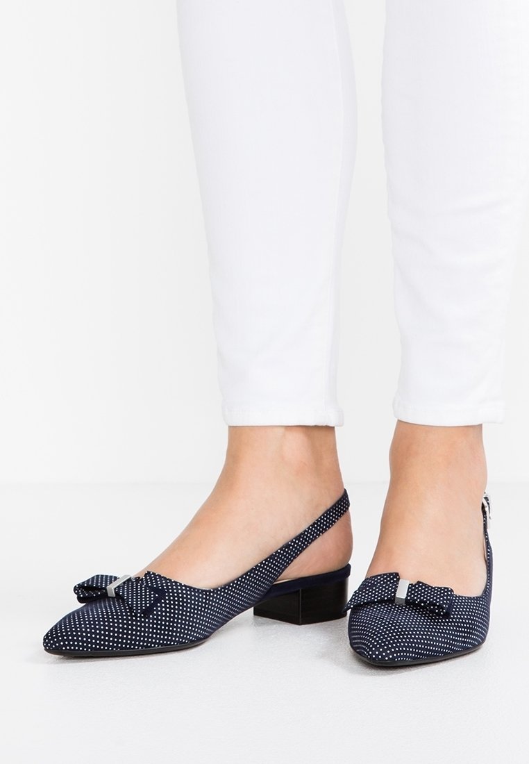 Bailarinas azul marino con tira trasera, diseño de lunares, punta afilada y detalle de lazo. Presentan un pequeño tacón cuadrado y una tela texturizada.