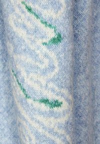 Helles blaues Strickgewebe mit einem weißen und grünen abstrakten Muster, das eine weiche Textur und ein leicht verschwommenes Aussehen aufweist.