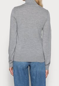 Pull à col roulé gris à manches longues, texture côtelée et coupe ajustée, associé à un jean large bleu clair.