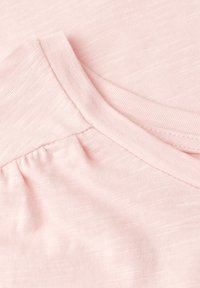 Gros plan sur un tissu doux rose montrant un détail de couture froncée et une texture lisse, mettant en valeur la construction du vêtement.