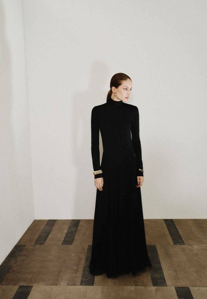 Vestido negro de manga larga con cuello alto, textura lisa y falda fluida. Acentos dorados notables en las mangas. Diseño minimalista.