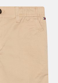 Béžové bavlněné šortky s hladkou texturou, s přední kapsou, zapínáním na knoflíky a malým logem v červené, bílé a modré barvě.