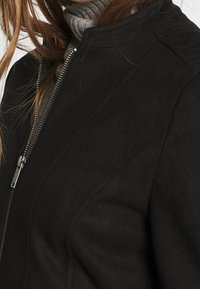 Giacca nera con zip, dal texture morbido, con colletto alto, design a cucitura diagonale e dettagli di cucitura sottili sulle spalle.
