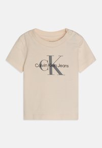 Beige puuvillainen t-paita, jossa on pyöreä pääntie, lyhyet hihat ja etupuolella harmaalla painettu "Calvin Klein Jeans" -logo.