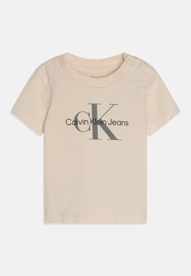 Beige puuvillainen t-paita, jossa on pyöreä pääntie, lyhyet hihat ja etupuolella harmaalla painettu "Calvin Klein Jeans" -logo.