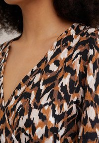 Tissu à imprimé léopard avec un mélange de teintes marron, noir et blanc. Caractérisé par un décolleté en V et une texture côtelée, mettant en valeur des motifs audacieux.