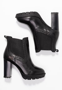 Botines negros de cuero y elástico, con tacón grueso, suela texturizada y detalles decorativos de recortes en los lados.