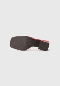 Rød sko med en teksturert svart såle og firkantet hæl. Har et solid design med en glatt overflate og synlig merkevaremønster på sålen.