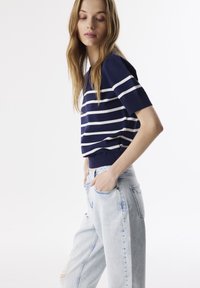Marineblauwe gestreepte sweater met witte horizontale strepen, korte mouwen en een aansluitende boord, gecombineerd met lichtblauwe versleten jeans.