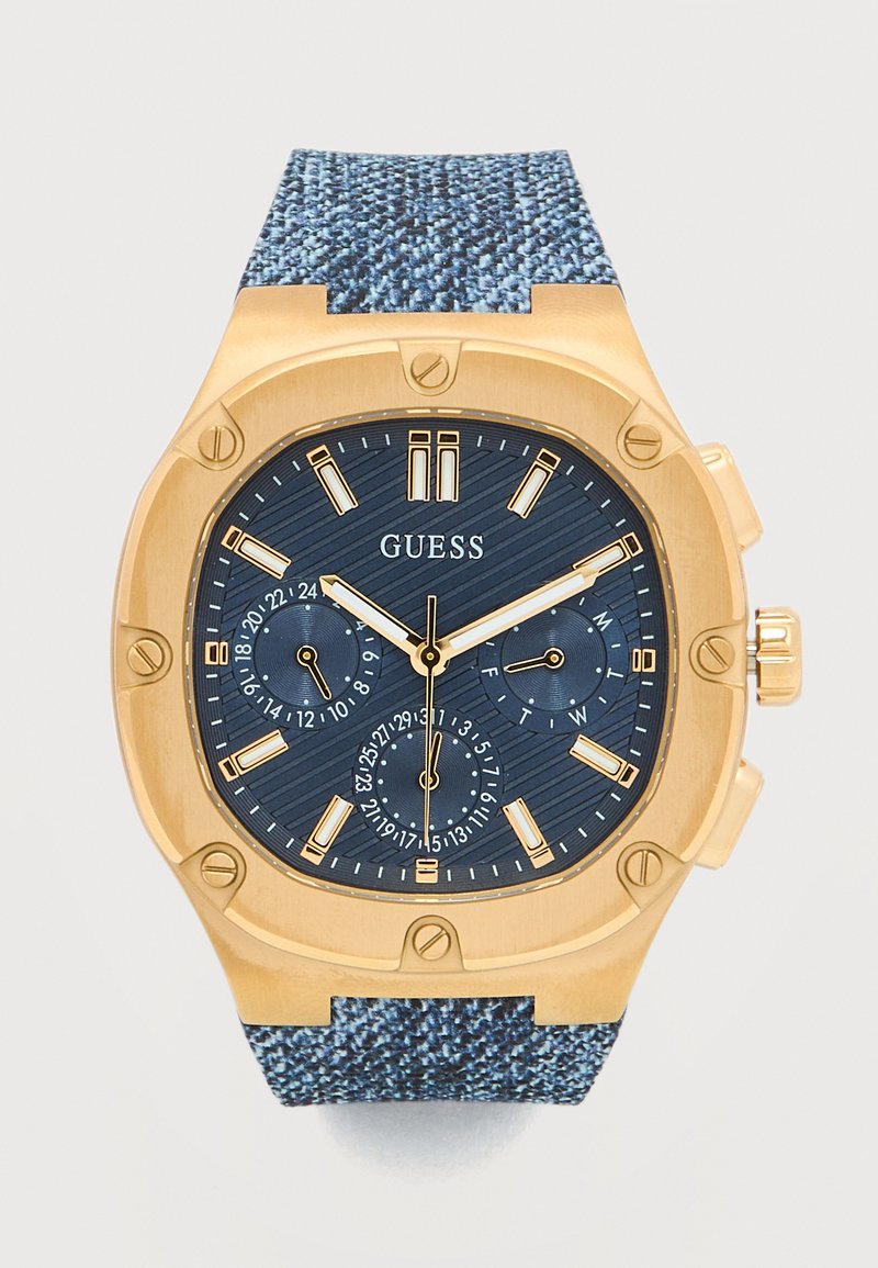 Ρολόι χειρός Guess με επίστρωση χρυσού, μπλε καντράν με υφή, τρεις υποκαντράν για 24ωρη ώρα, ημέρα και ημερομηνία, και μπλε υφασμάτινο λουράκι.