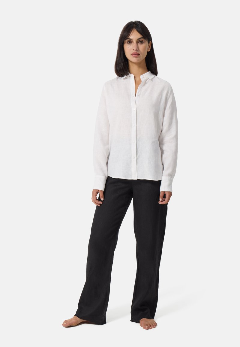 Chemise blanche en lin à manches longues avec un col, fermeture par boutons et coupe décontractée, associée à un pantalon noir à jambes larges.