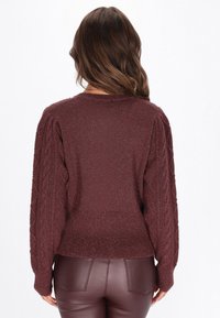 Burgundský pletený svetr s rukávy v kabelkovém vzoru, texturovaná látka a žebrovaný lem. Nosené s lesklými hnědými legínami podobajícími se kůži.