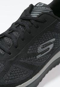 Černá teniska Skechers s pletenou tkaninou, šněrovacím designem, šedým logem "S" na boku a polstrovanou podrážkou.