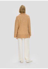 Maglione oversize beige con colletto, maniche lunghe e orlo a costine, abbinato a pantaloni larghi color avorio e sneaker bianche.