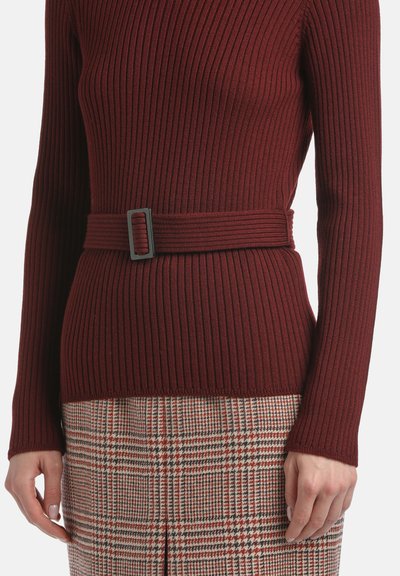 Pull en maroon côtelé avec un design ajusté, doté d'une ceinture en tissu assortie et d'une finition texturée, associé à une jupe à carreaux.