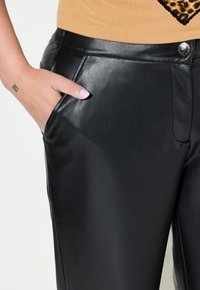 Pantaloni in ecopelle nera con una texture liscia, dotati di una tasca frontale e dettagli in metallo lucido sulla vita.