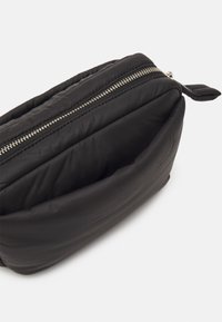 Borsa nera imbottita con una finitura lucida, dotata di chiusura con zip superiore e di una piccola etichetta in tessuto sul lato.