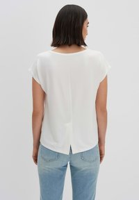 Top bianco a maniche corte con scollo rotondo e dettaglio di cucitura sul retro. Abbinato a jeans azzurri, presenta un outfit casual.