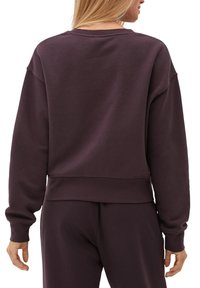 Felpa di colore viola scuro con tessuto morbido e strutturato. Presenta una scollatura tonda, spalle scese e una vestibilità corta. Design semplice.