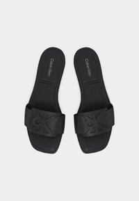 Paire de sandales Calvin Klein noires à enfiler, avec larges brides présentant un logo découpé, semelle plate et bout carré.
