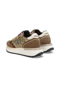 Un paio di sneakers marroni con lati glitter dorati, lacci viola, dettagli a stampa animale e suole bianche spesse, rivolte all'indietro su uno sfondo bianco.