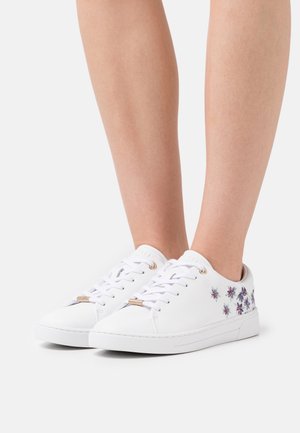 Zapatillas blancas de cuero con bordado floral en morado y azul, punta redonda, estilo con cordones y detalles de herrajes en tono dorado.