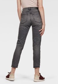 Jeans ajustados en denim gris oscuro con cintura alta, bolsillos traseros y un ligero ajuste en los tobillos. Combinados con zapatillas bajas.