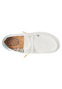 Zapato de lona blanco sin cordones con una parte superior texturizada, plantilla de corcho, acentos naranjas y un forro con un patrón colorido.