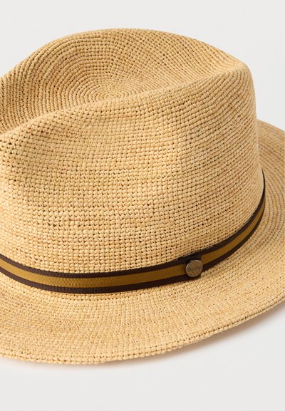 Μπεζ ψάθινο καπέλο με υφαντή υφή, διακοσμημένο με καφέ κορδέλα και μεταλλικό κουμπί γύρω από την κορώνα.