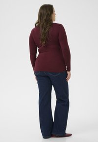 Bordeaux langemouwige top met geribbelde textuur, gecombineerd met donkerblauwe wijde jeans. Eenvoudig ontwerp zonder opvallende versieringen.