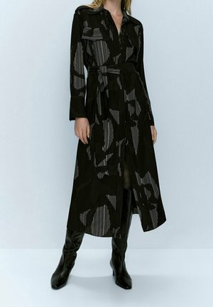 Black long-sleeve dress with vertical stripes and large abstract patterns, cinched at the waist with a matching belt. Smooth fabric texture.