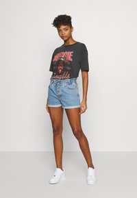 T-shirt graphique noir avec le texte "Biggie Smalls", associé à un short en denim bleu clair taille haute avec un devant à boutons et des ourlets retroussés.