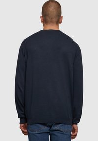 Mørkeblå strikkegenser med rund hals og lange ermer. Har ribbestrikkede mansjetter og kant, glatt tekstur og avslappet passform.
