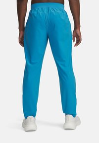 Lyseblå træningsbukser med elastisk talje, der har en glat overflade og tapered pasform, parret med hvide sneakers.