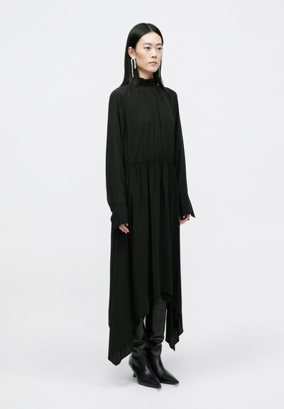 Čierne šaty s dlhým rukávom, s naťahovaným pásom, asymetrickým lemom a širokými rukávmi. V páre s ostrými čiernymi čižmami. Hladká textúra.