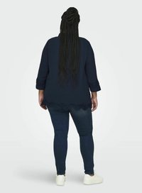 Maglietta a maniche lunghe blu navy con dettagli in pizzo sull'orlo, abbinata a jeans skinny in denim scuro e sneaker bianche, vista da dietro.