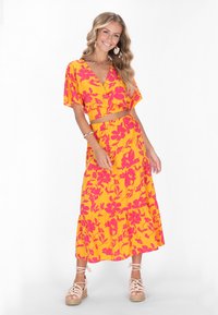 Gelbes Blumen-Zweiteiler-Outfit mit einem bauchfreien Oberteil mit ellenlangen Ärmeln und einem gestuften Maxirock mit elastischem Bund.