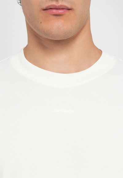 Hvit crew neck t-skjorte laget av bomull, med en subtil preget logo "SANDRO" på brystet, med jevn tekstur og minimal design.
