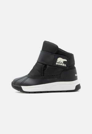 Bota de invierno negra de caña alta con suela blanca, cierre de velcro y logo de Sorel con un oso polar en el lateral.