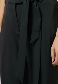 Black tailored trousers made from smooth fabric, featuring a tied belt, side pockets, and pleated details on the front.