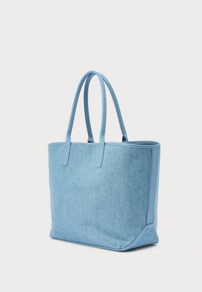 Τσάντα ώμου από ανοιχτό μπλε τζιν με ταιριαστές μπλε δερμάτινες χειρολαβές και περιθώρια, όρθια σε λευκό φόντο.