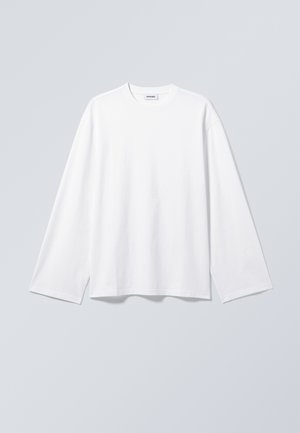 T-shirt blanc uni à manches longues avec col rond et coupe décontractée, suspendu sur un fond gris clair.