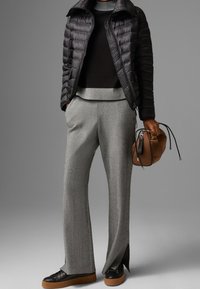 Svart puffjacka, grå tröja, grå vida byxor och svarta skor med bruna sulor. Brun väska med dragsnörningsdetalj.