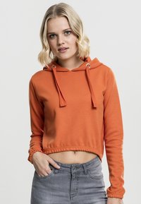 Hanorac scurt portocalie cu ochiuri argintii, sireturi și tiv ondulat; purtat cu blugi gri din denim. Textură netedă și mâneci lungi.