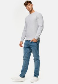 Pull en maille texturée gris, col rond, manches longues, associé à un jean en denim bleu et des baskets blanches. Design simple et décontracté.