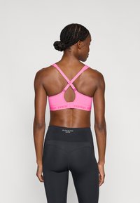 Ροζ αθλητικό σουτιέν με υφασμένο σχέδιο και σχεδιασμό με σταυρωτή πλάτη, διαθέτει ρυθμιζόμενους ιμάντες και ταινία με λογότυπο. Συνδυάζεται με μαύρο κολάν ψηλόμεσο.