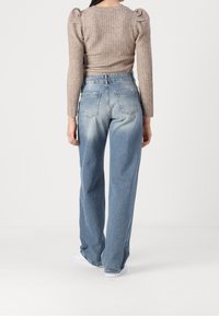 Light brown ribbed long-sleeve top with puffed shoulders paired with high-waisted, light blue wide-leg jeans featuring fading and back pockets.
